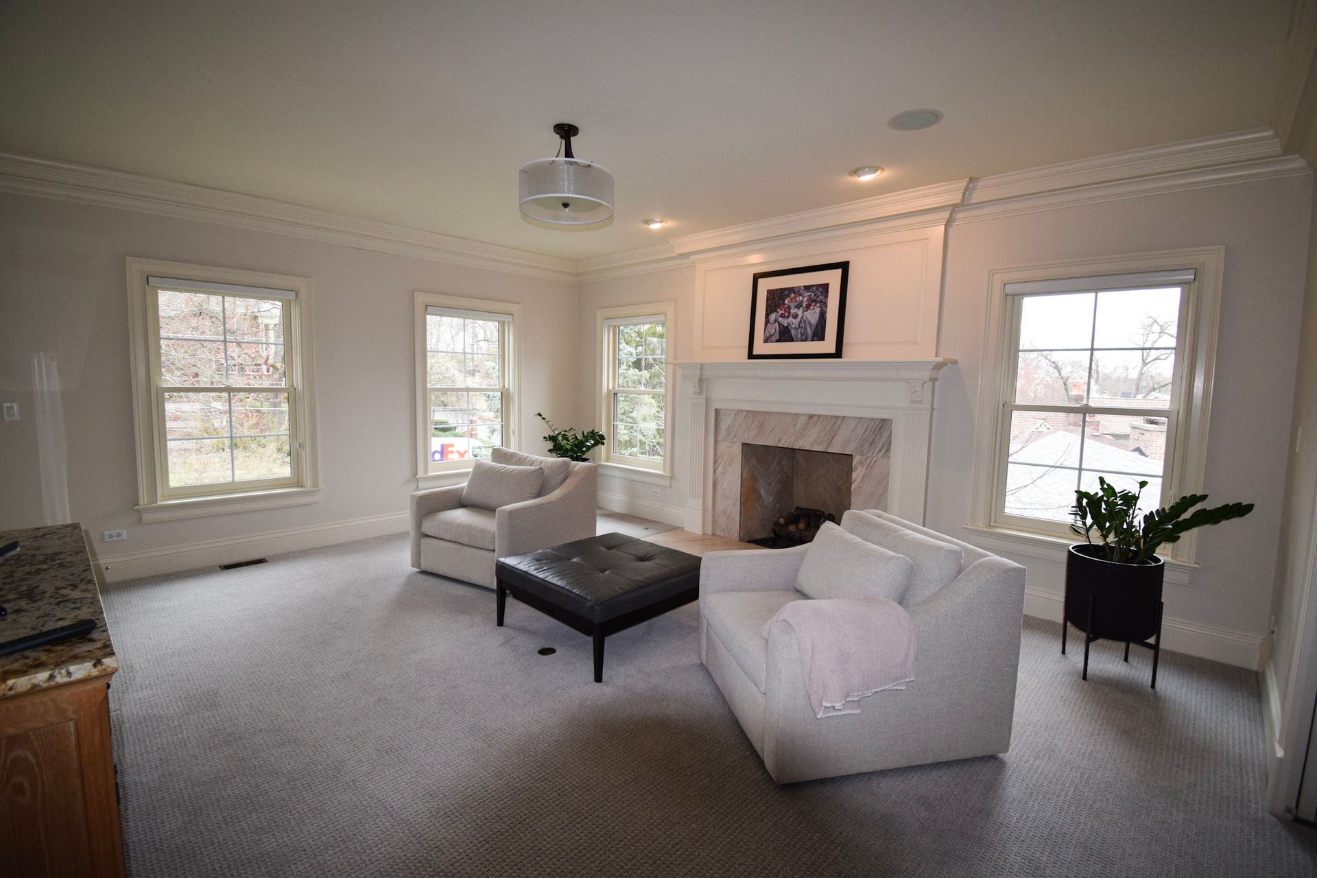 Spacious living room with white walls, fireplace, and two armchairs; a dark ottoman sits between them.