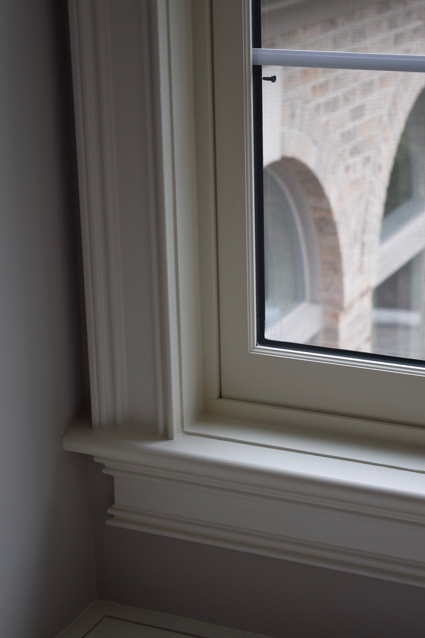 Corner of a window with white trim and a screen. The wall is painted a light purple color.