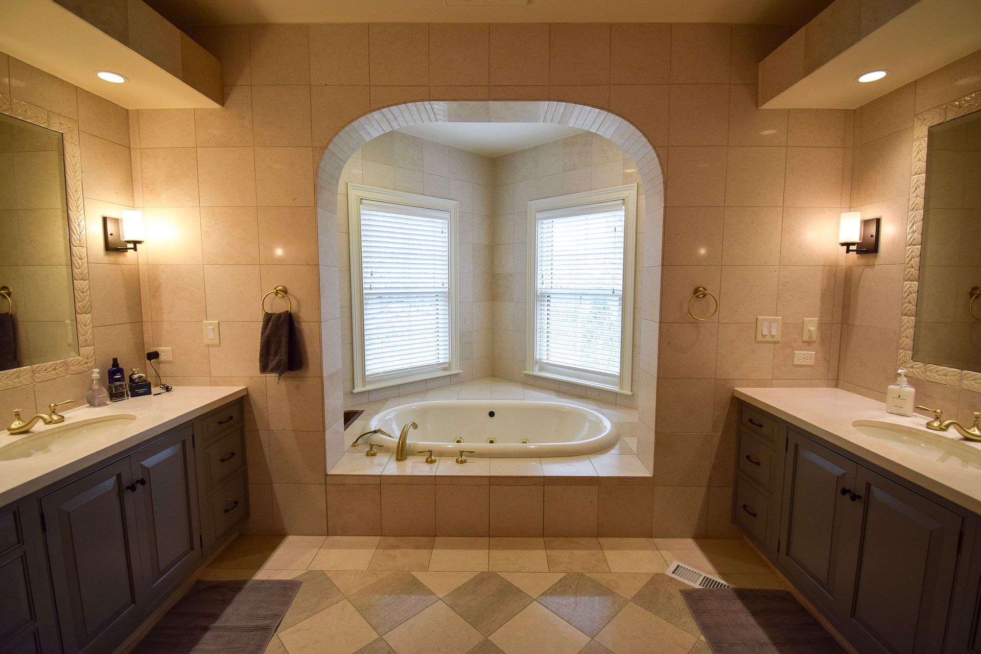Luxury bathroom with double sinks, centered tub alcove, and neutral tiles.
