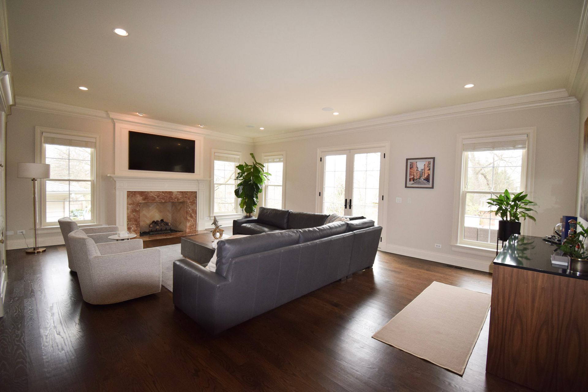 Spacious living room with a fireplace, dark gray sectional, white armchairs, and large windows.