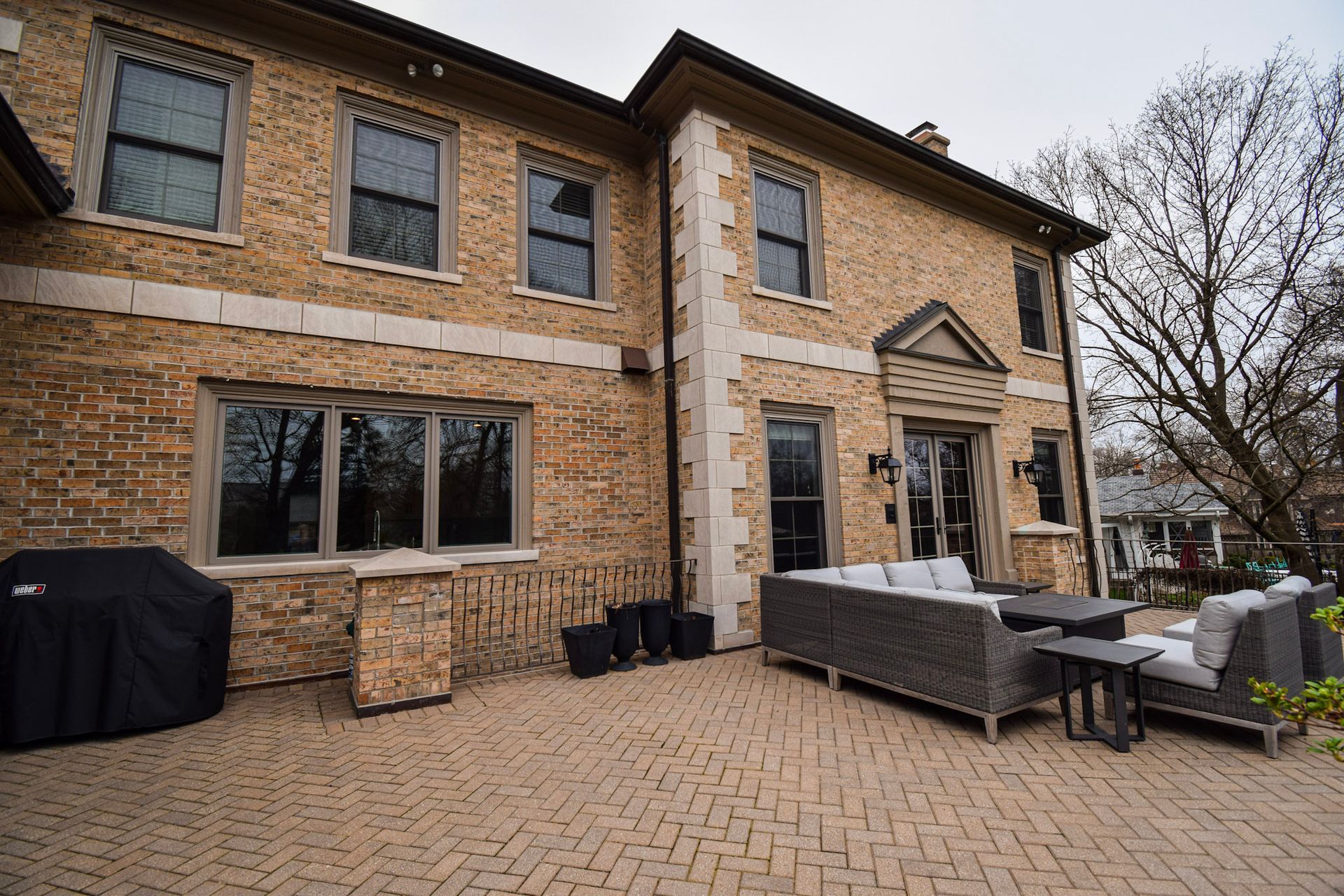 Brick house with patio furniture. Brown brick facade, stone trim. Cloudy day.