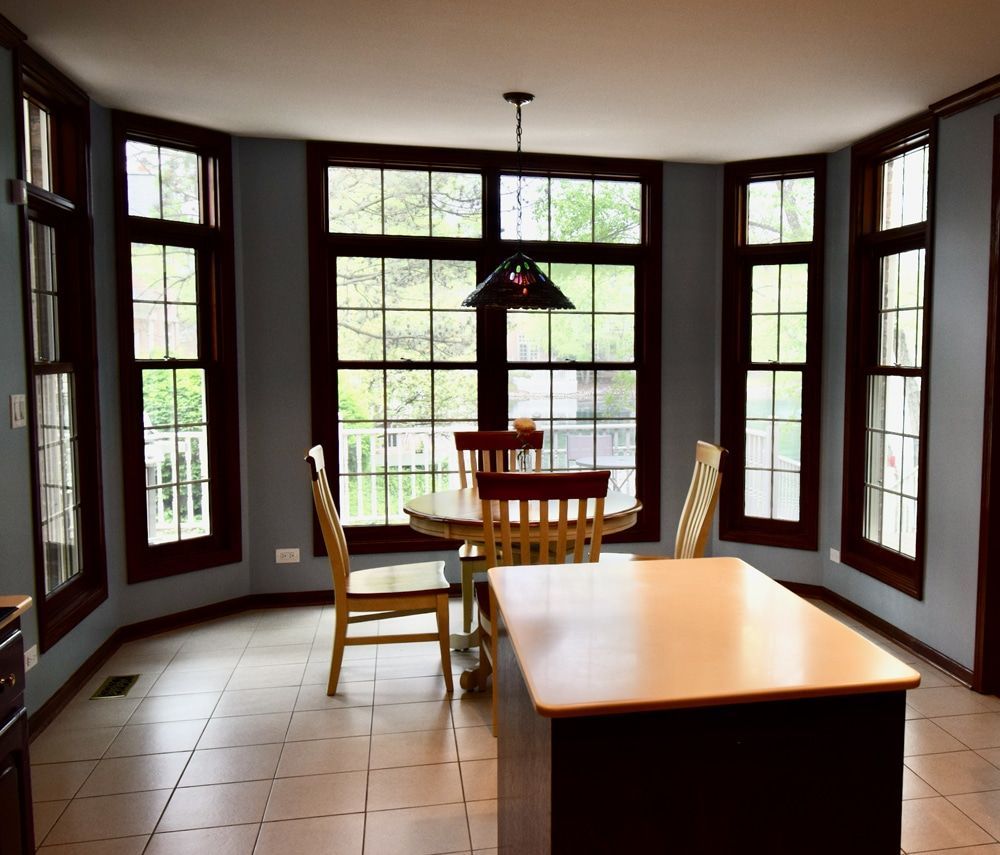 A dining room with a table and chairs and lots of windows