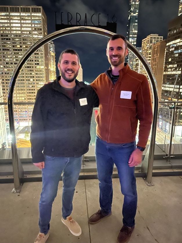 Two men are standing next to each other on a rooftop at night.