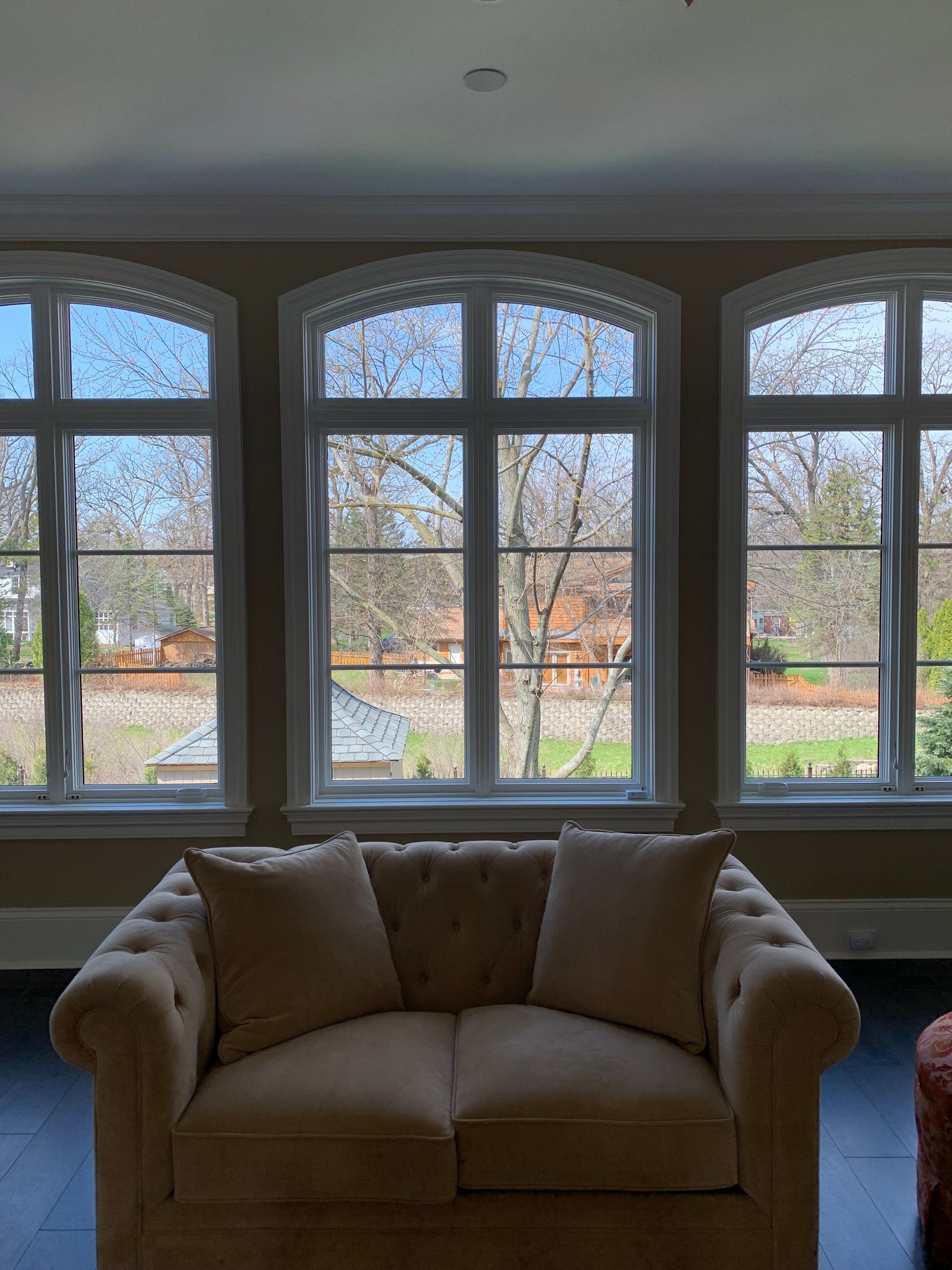 Beige sofa in front of three arched windows with a view of trees.