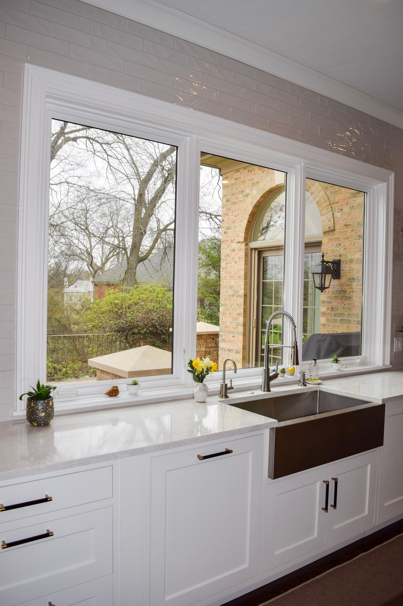 White kitchen with a large window overlooking a garden. Stainless steel sink, white cabinets, and a granite countertop.