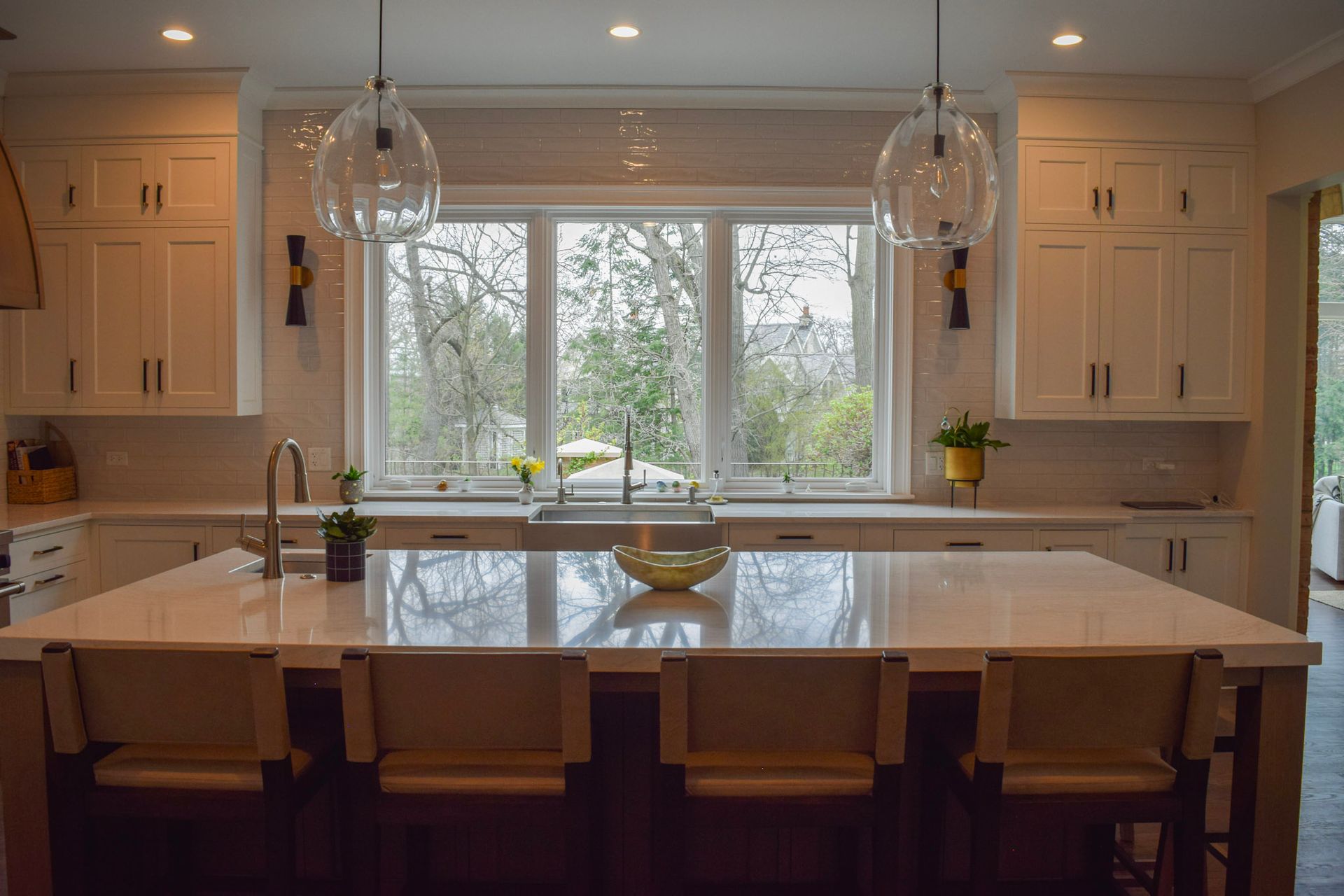 Spacious, bright kitchen with white cabinets, large island with seating, and a window overlooking trees.