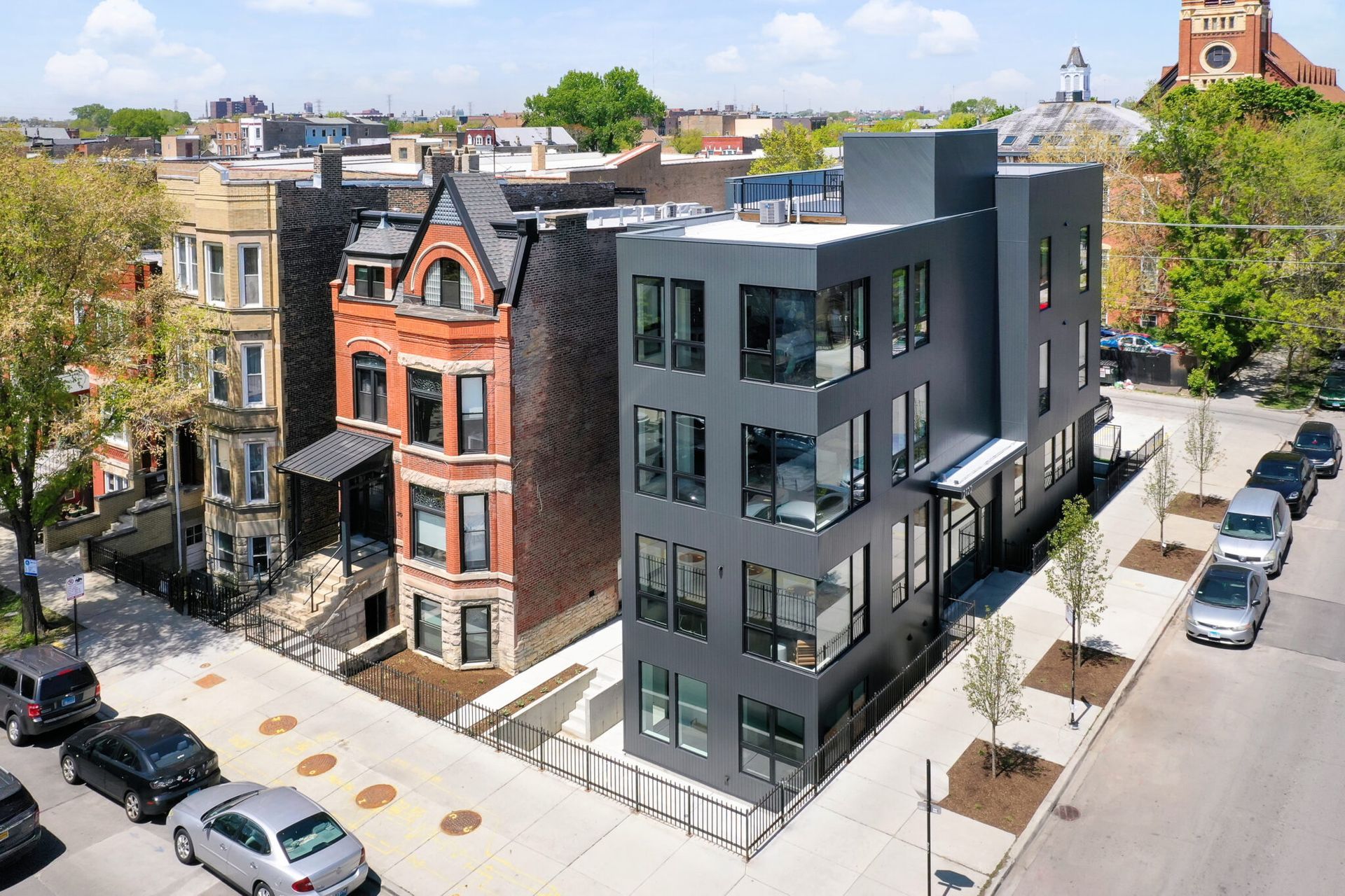 A modern dark gray three-story building next to older brick buildings in a city street setting.
