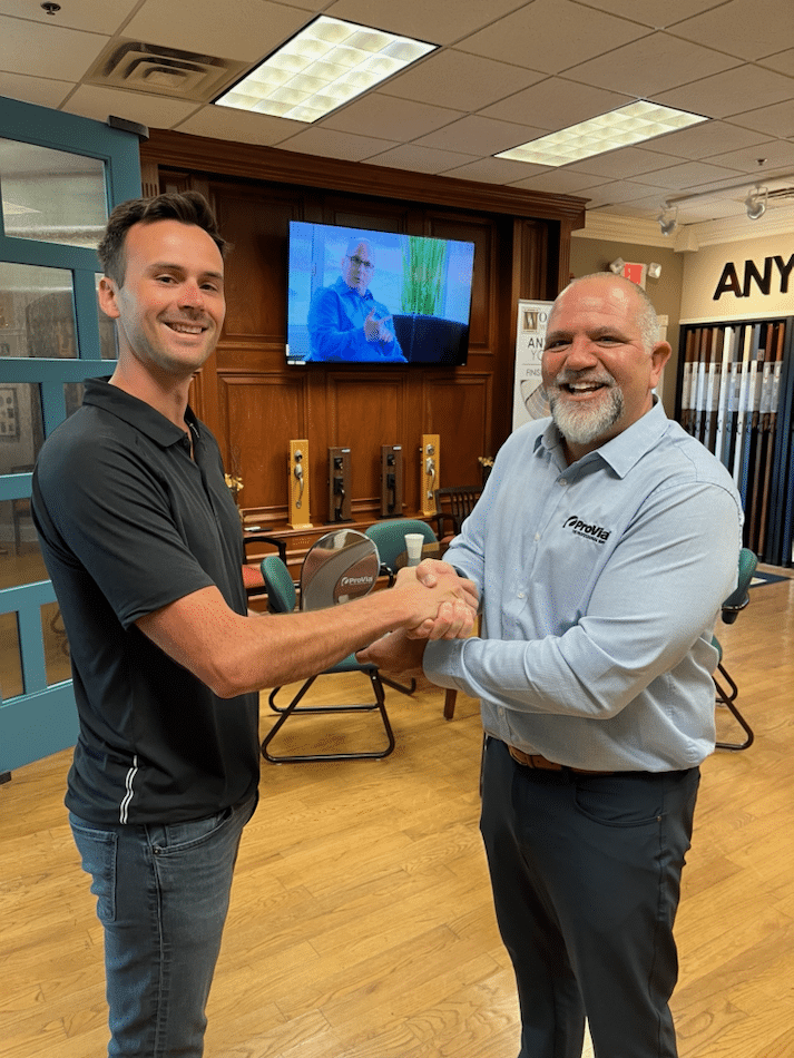 Two men are shaking hands in a room in front of a television.