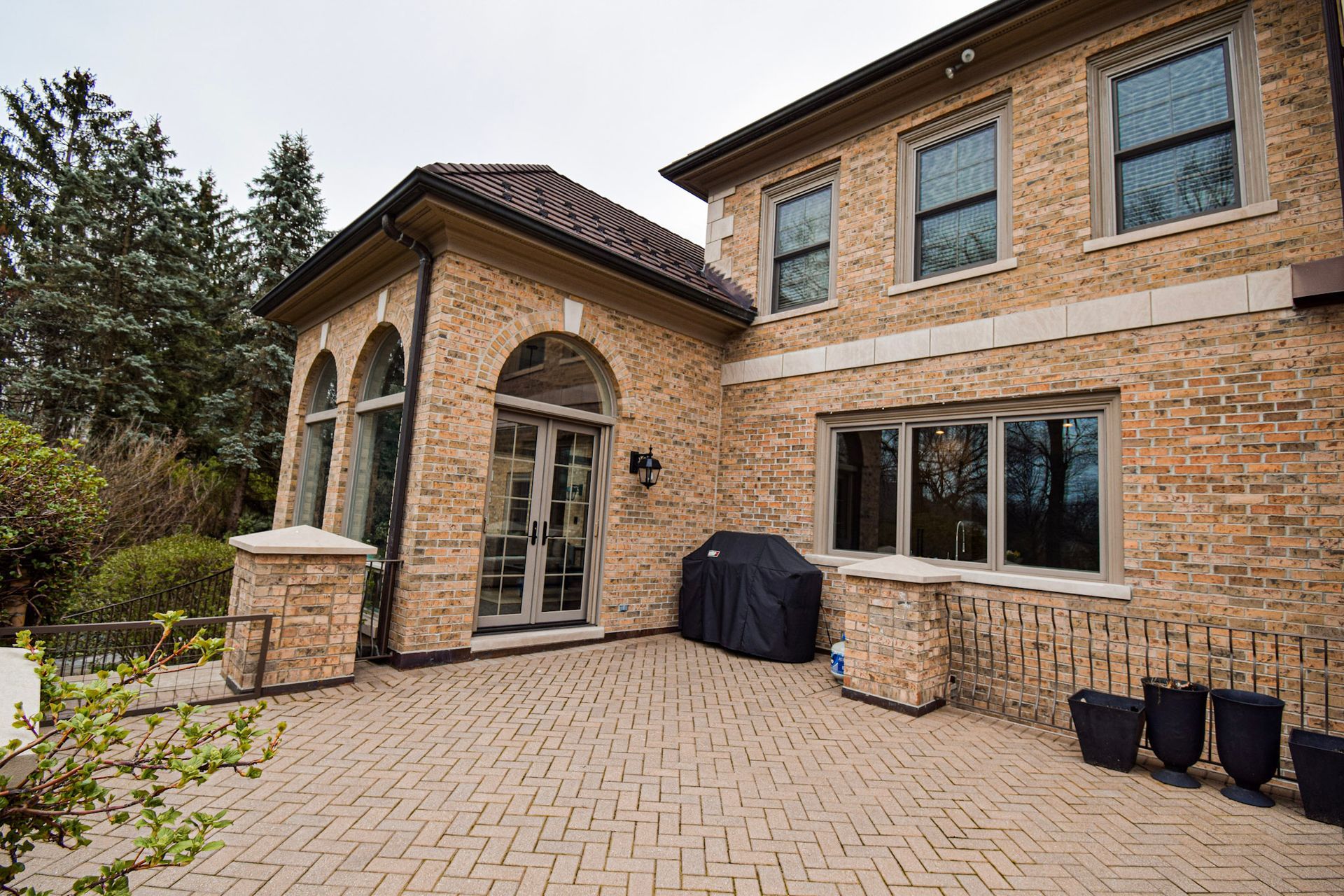 Back patio of brick house with arched doorway, grill, and paved brick surface.