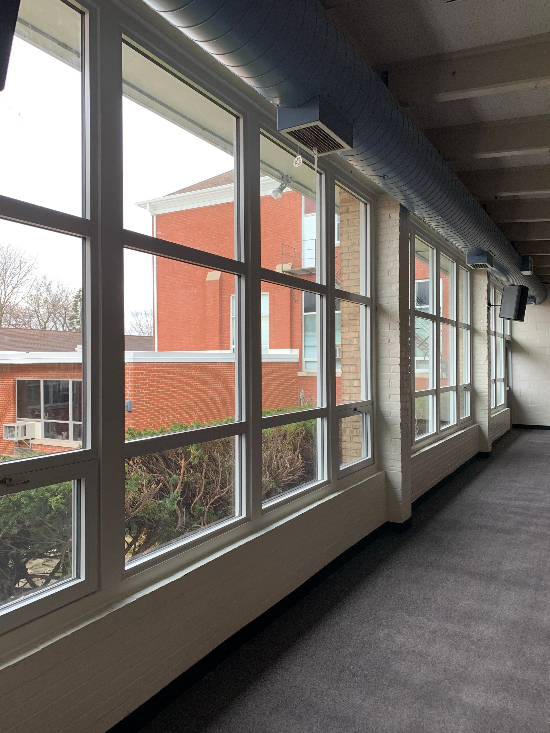 Hallway with a series of rectangular windows looking out to a brick building on a cloudy day.
