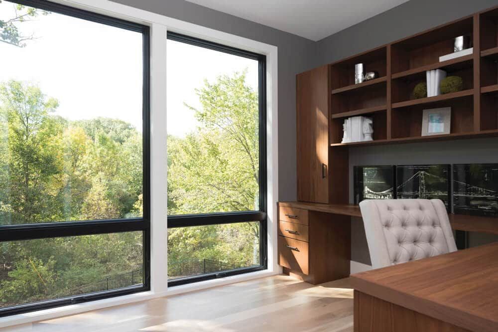 A home office with a desk , chair , shelves and lots of windows.