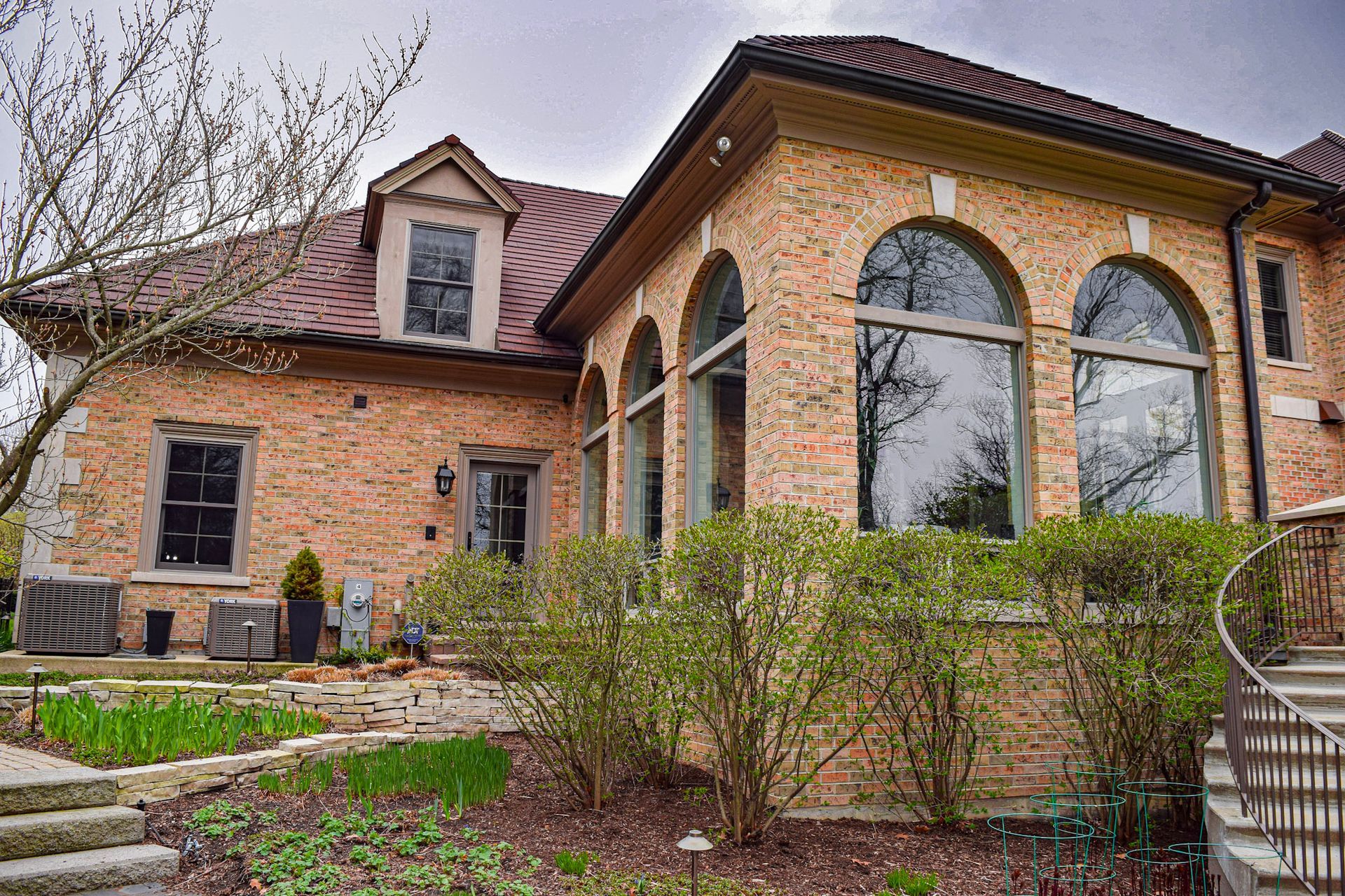 Brick house with arched windows, red tile roof, and landscaping.