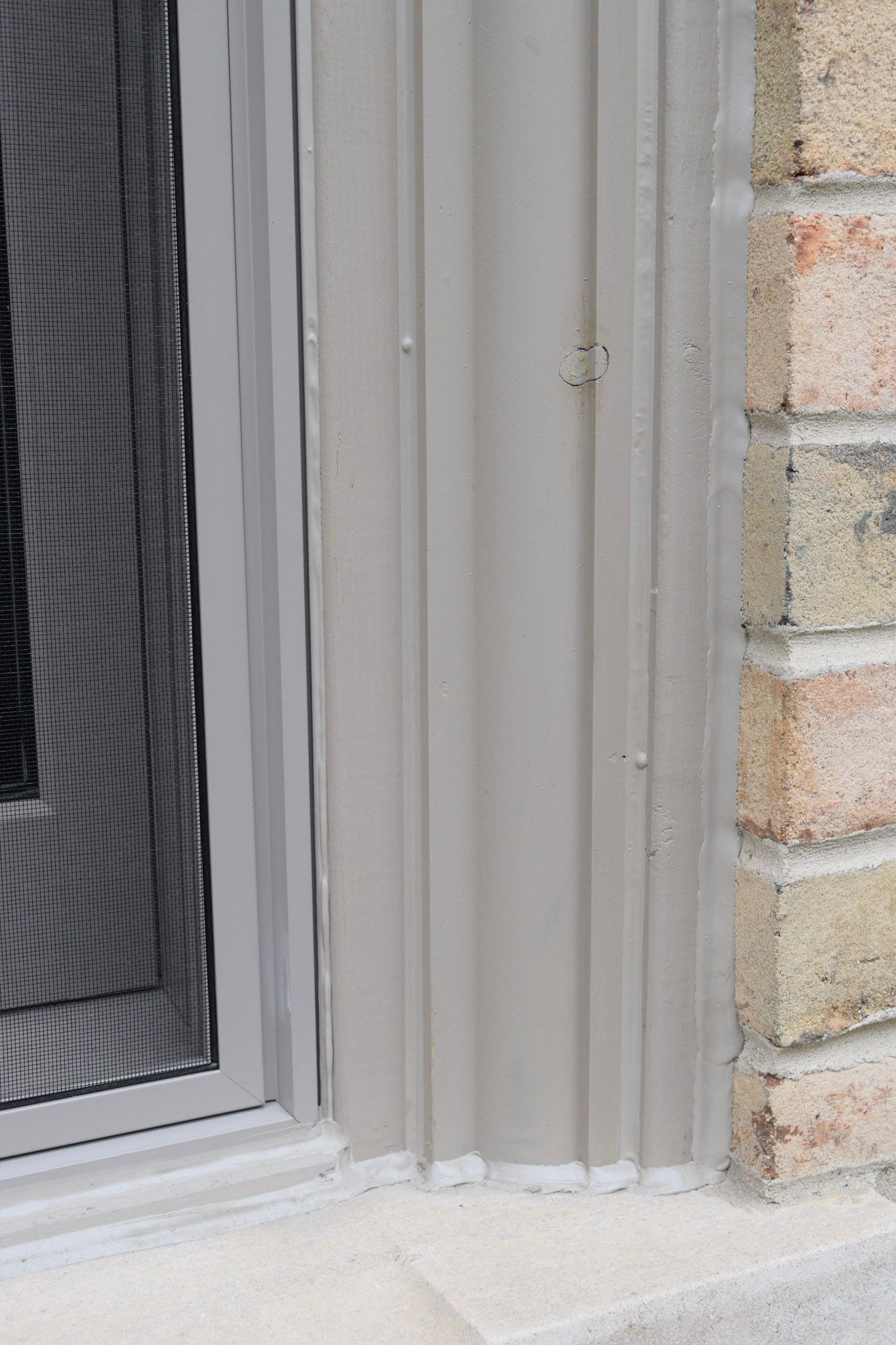 Beige fluted trim around a window, next to red brick.
