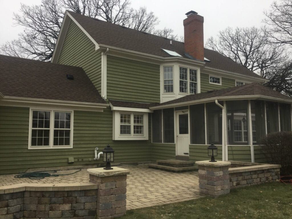 A green house with a brown roof and a screened in porch