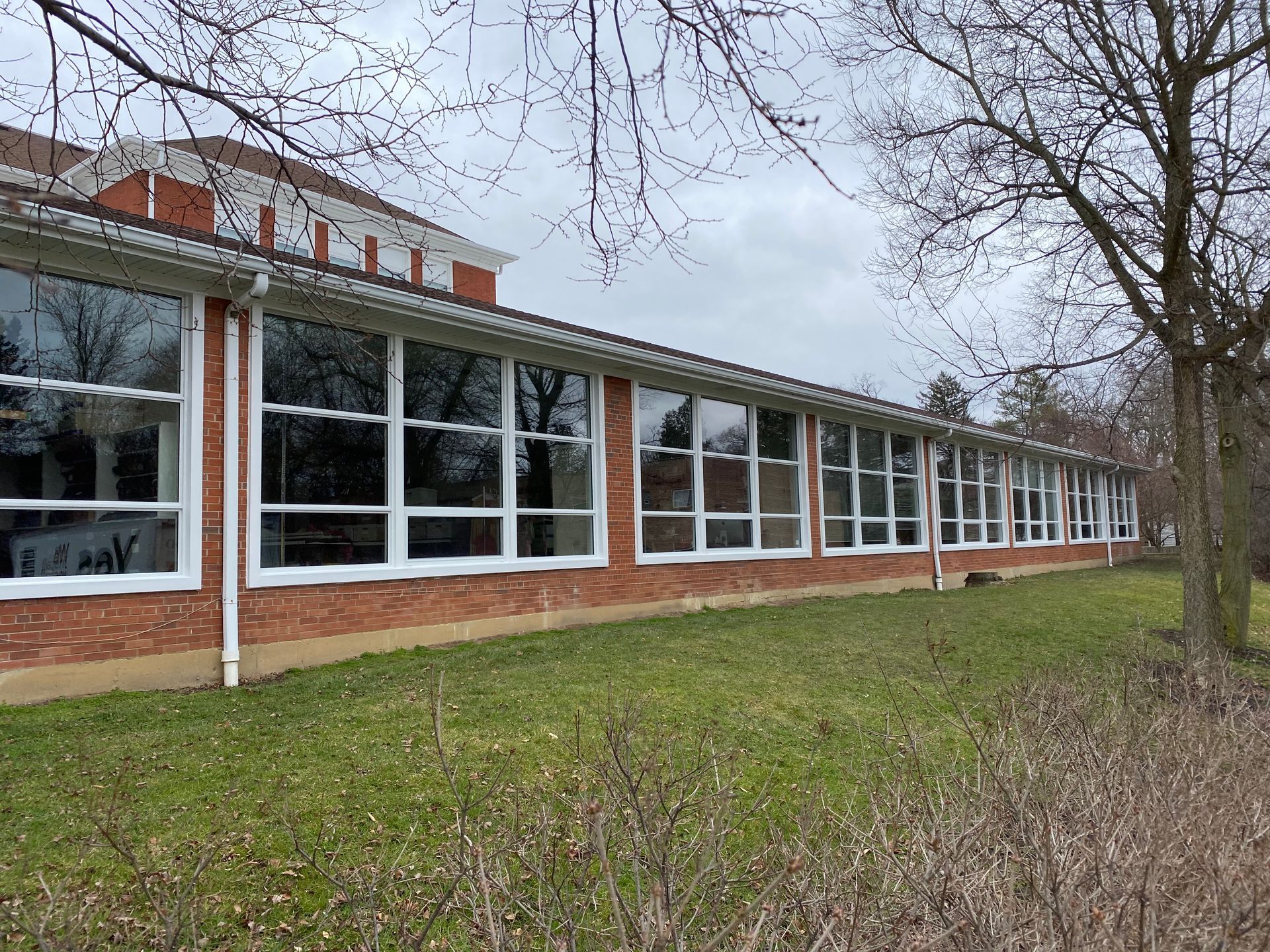 Brick building with long row of windows, white frames, and green grass in front.
