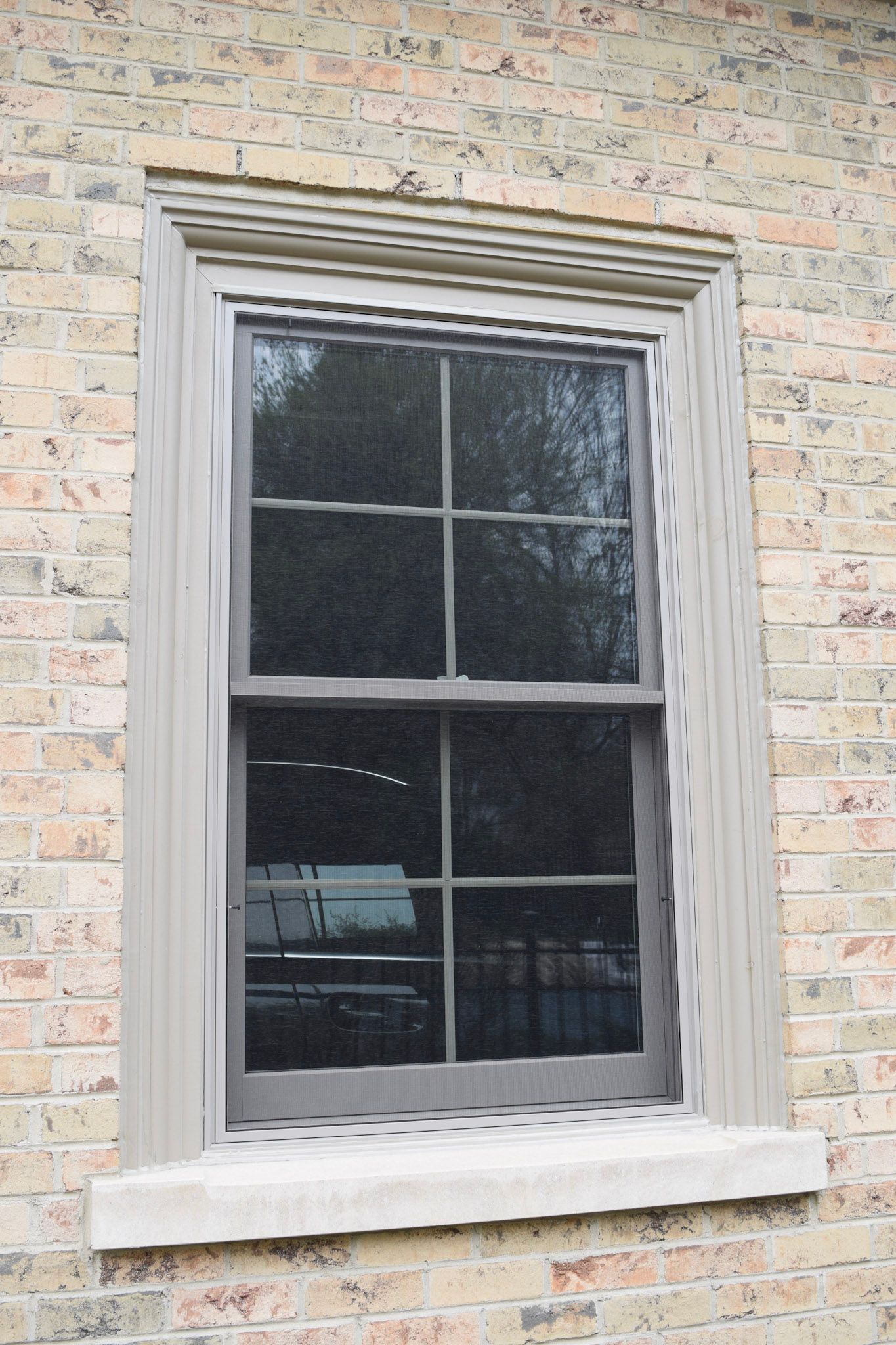 Tall gray-framed window on a brick building, with a stone windowsill and decorative molding.