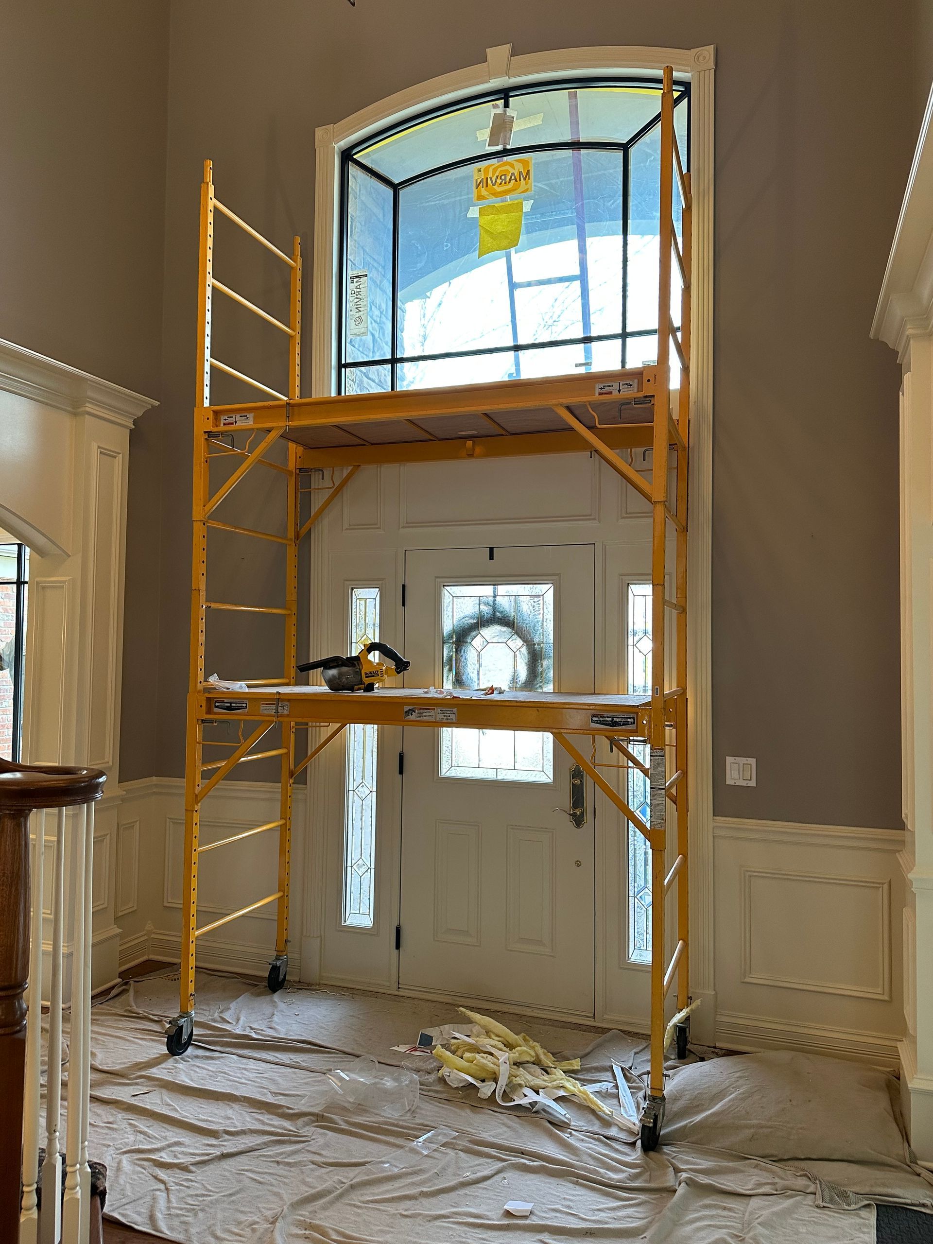 Yellow scaffolding in a foyer; door in background. Tools and debris on platform and floor.