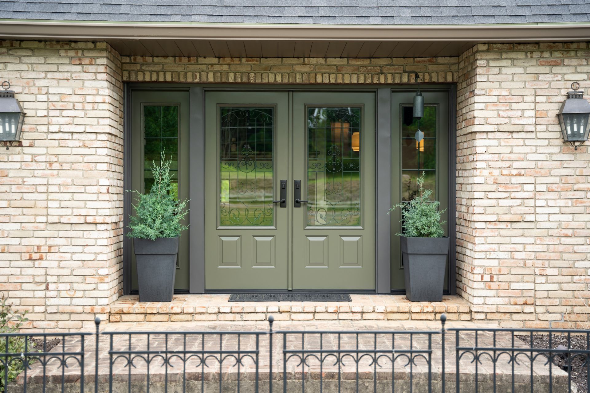 A brick house with green doors and potted plants in front of it.