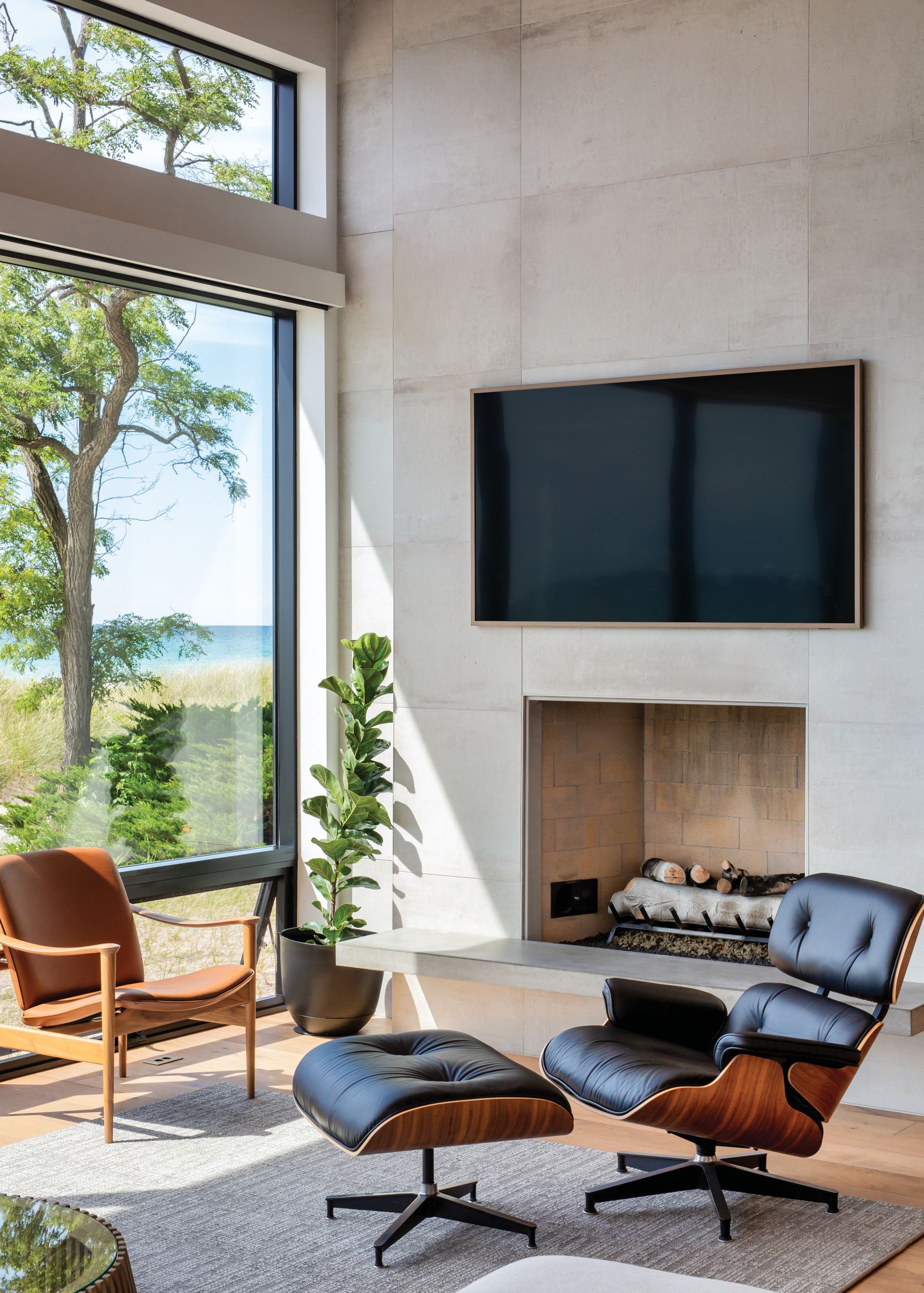A living room with a fireplace , chairs , ottoman and television.
