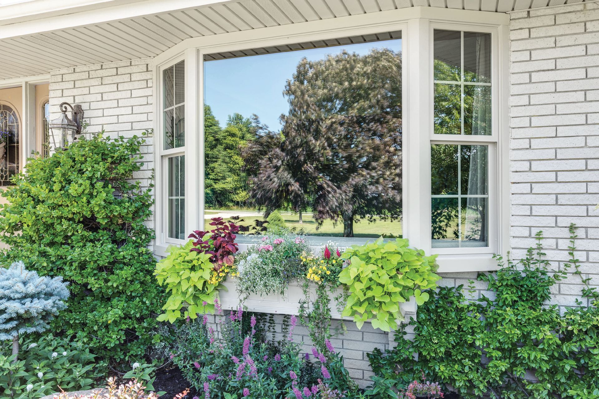 A white brick house with a large bay window and flowers in front of it.