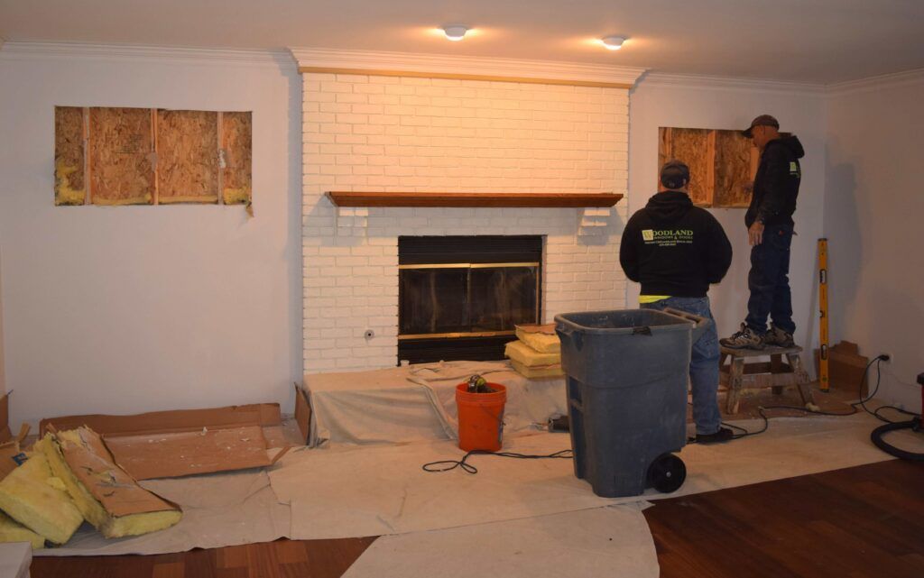 Two men are working on a fireplace in a living room.