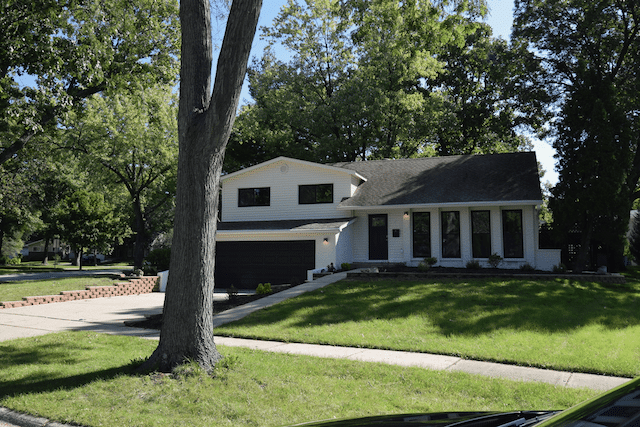 A white house with a black garage door is surrounded by trees and grass.