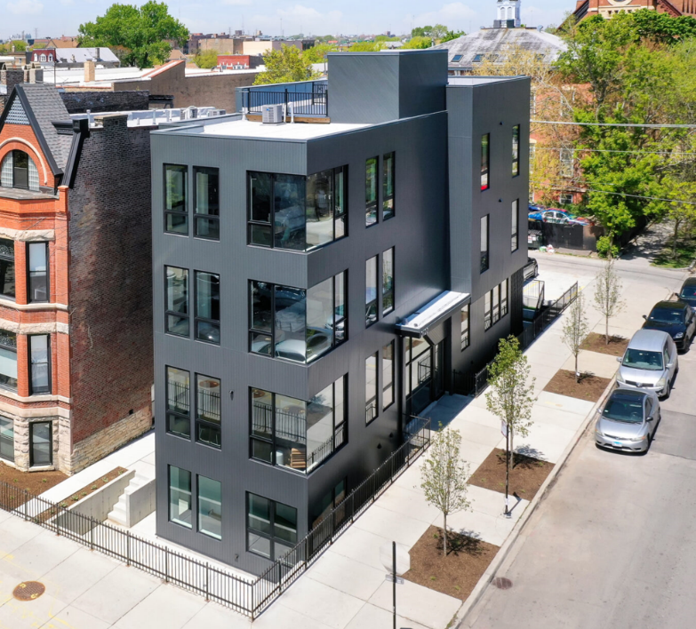 A two-story brick mansion with white columns, a large triangular pediment, and black shutters, set among trees and shrubs.