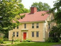 A large yellow house with a red roof and a red door surrounded by trees.