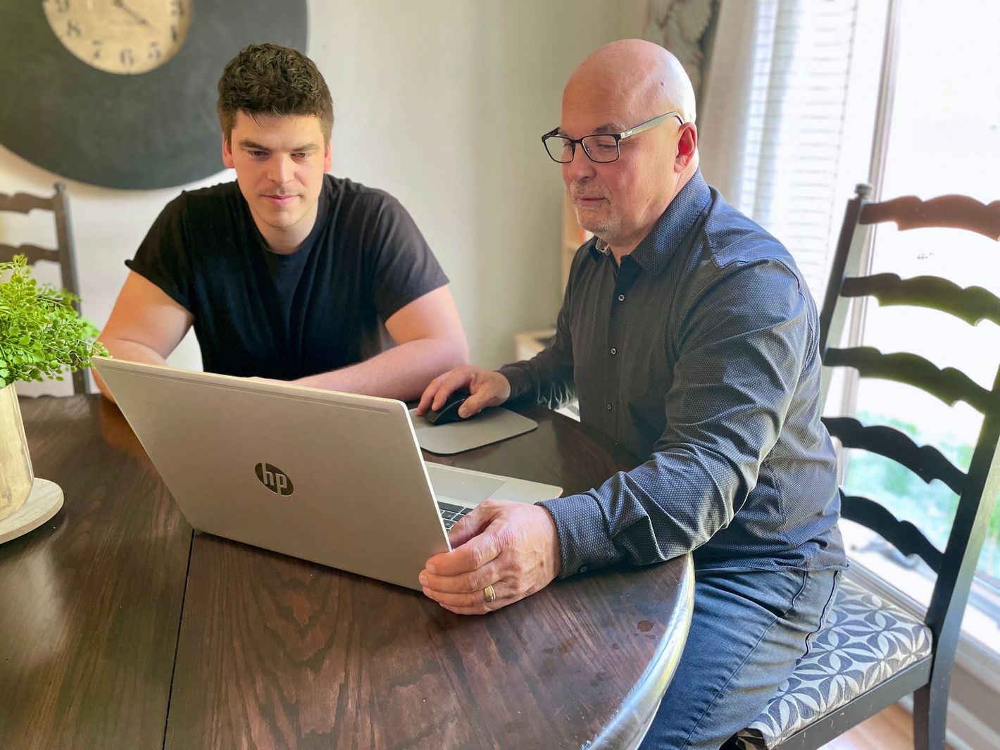 Two men are sitting at a table looking at a laptop computer.