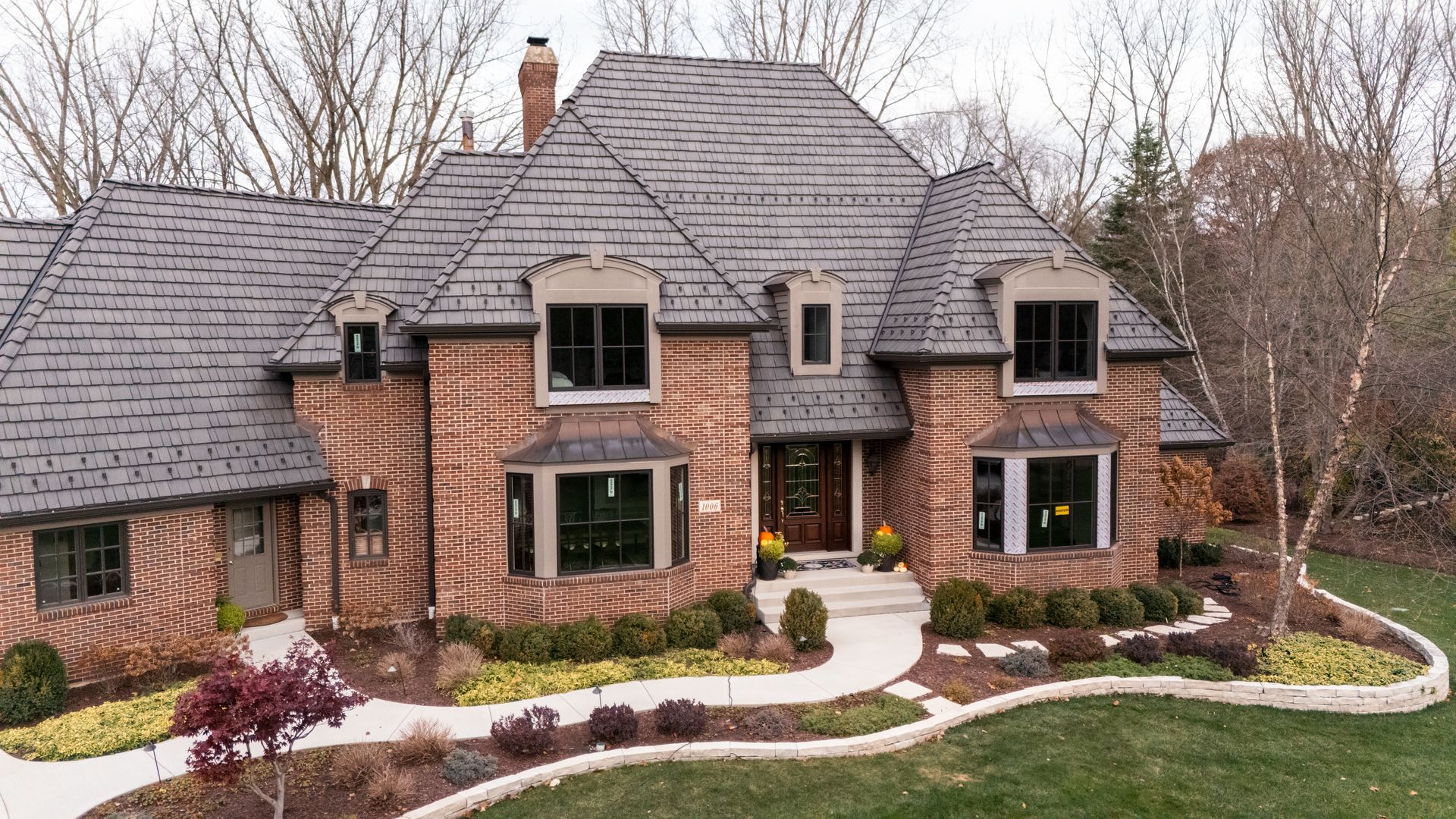 Brick house with a dark roof, featuring arched windows and landscaped lawn.