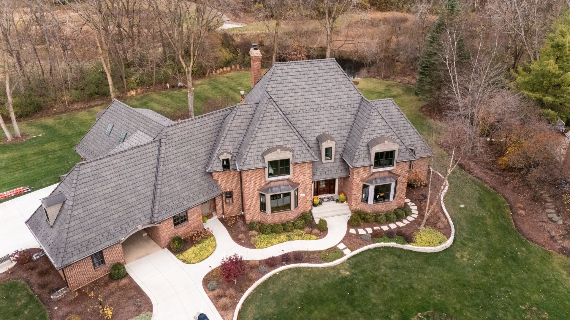 Brick house with gray roof, surrounded by green grass and trees.