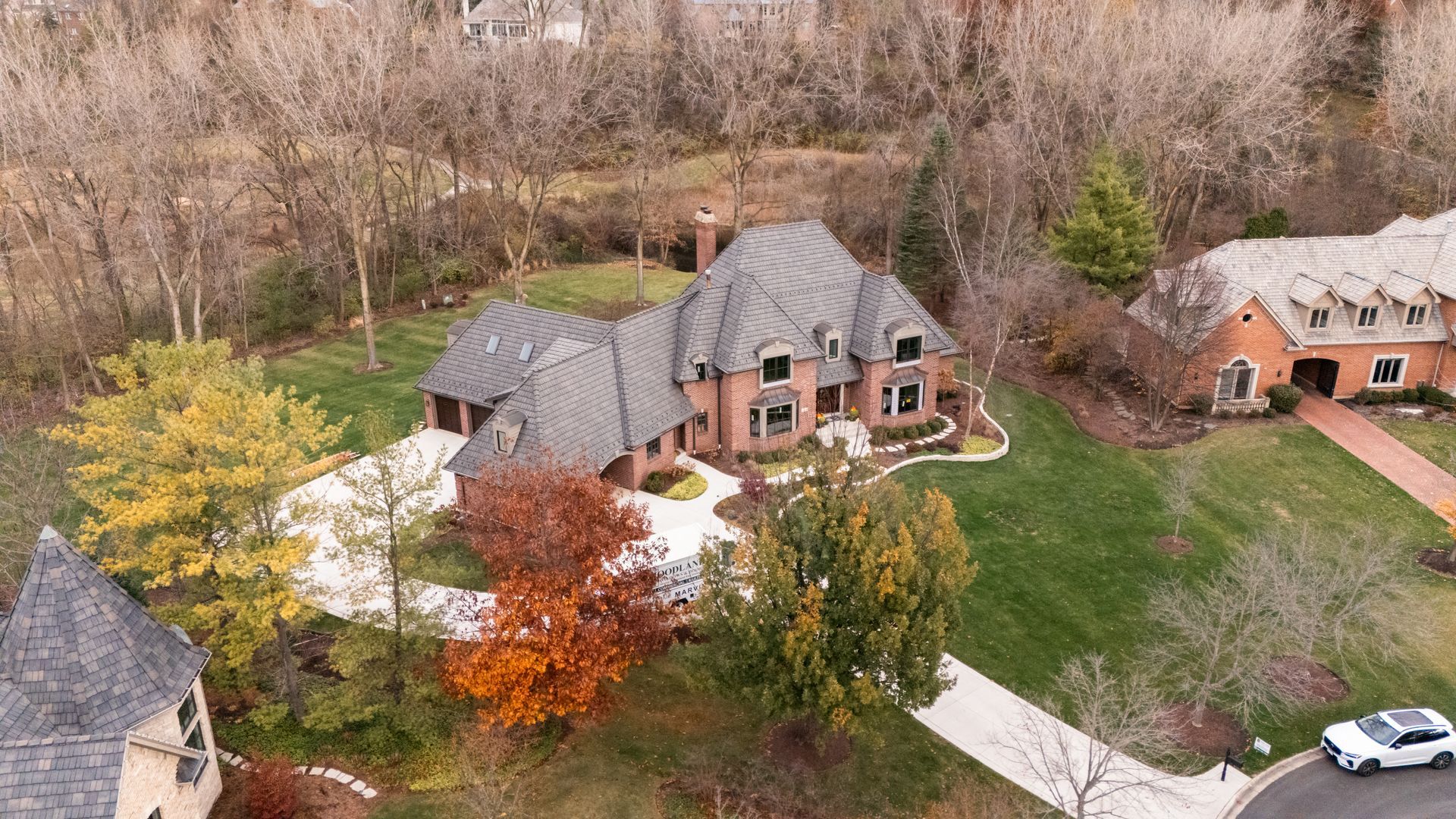 Aerial view of a large brick house with a winding driveway and trees with fall foliage.