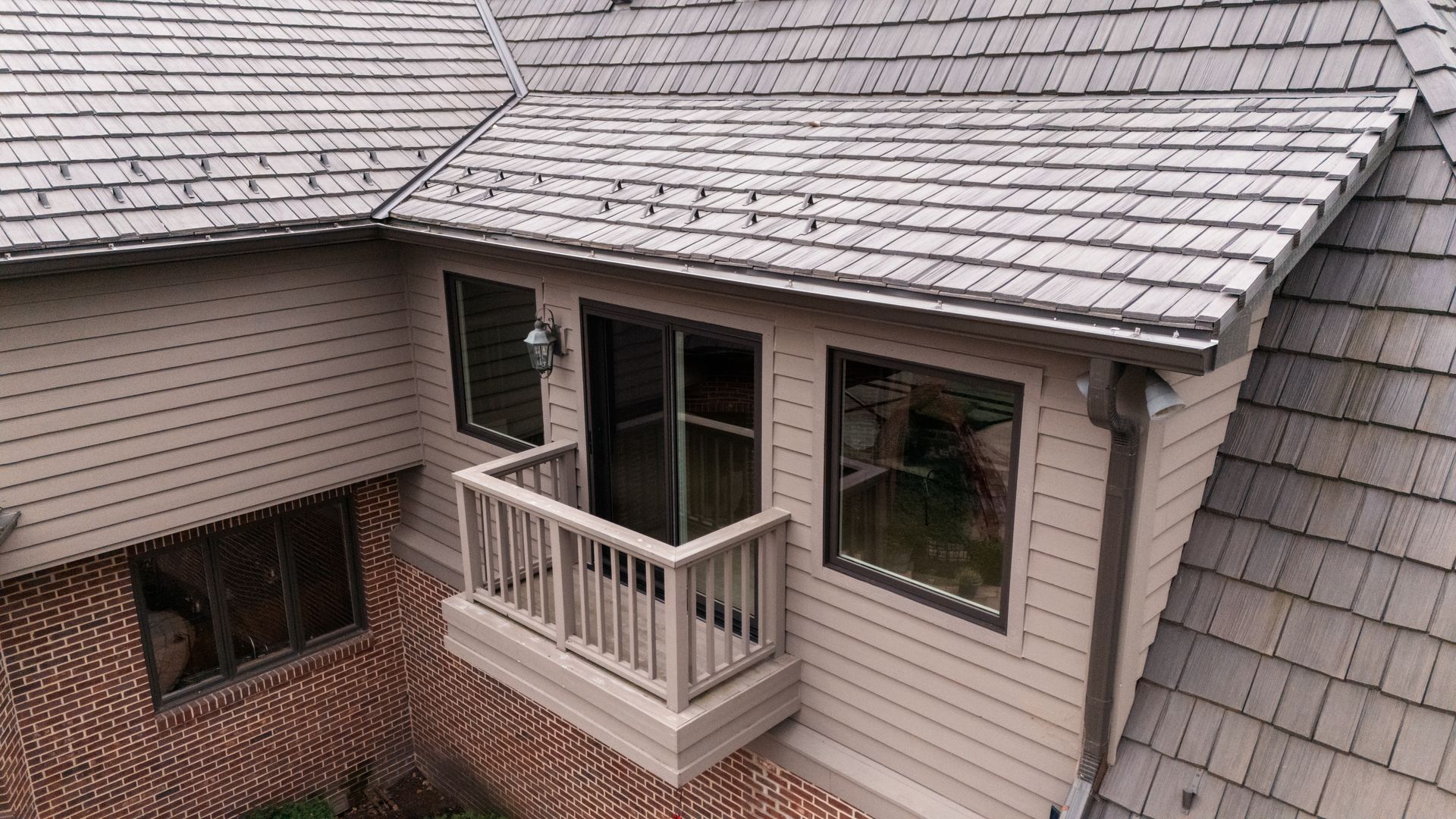 Tan house with a wooden shingle roof, balcony, and windows.