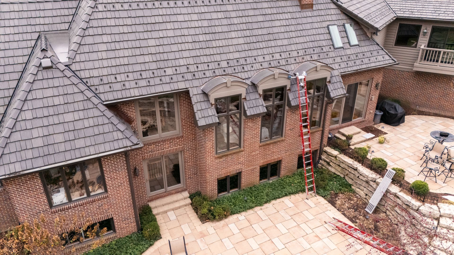 Brick house with gray roof; red ladder leans against the building.
