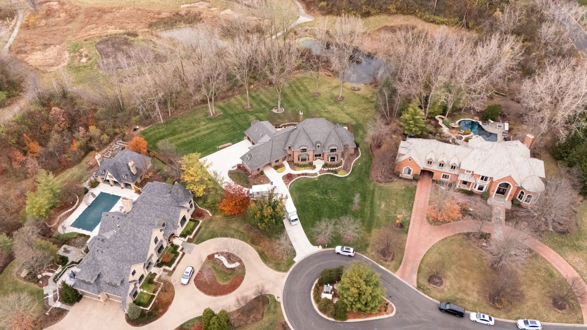 Aerial view of several large houses on a green, tree-lined lot with a winding road.