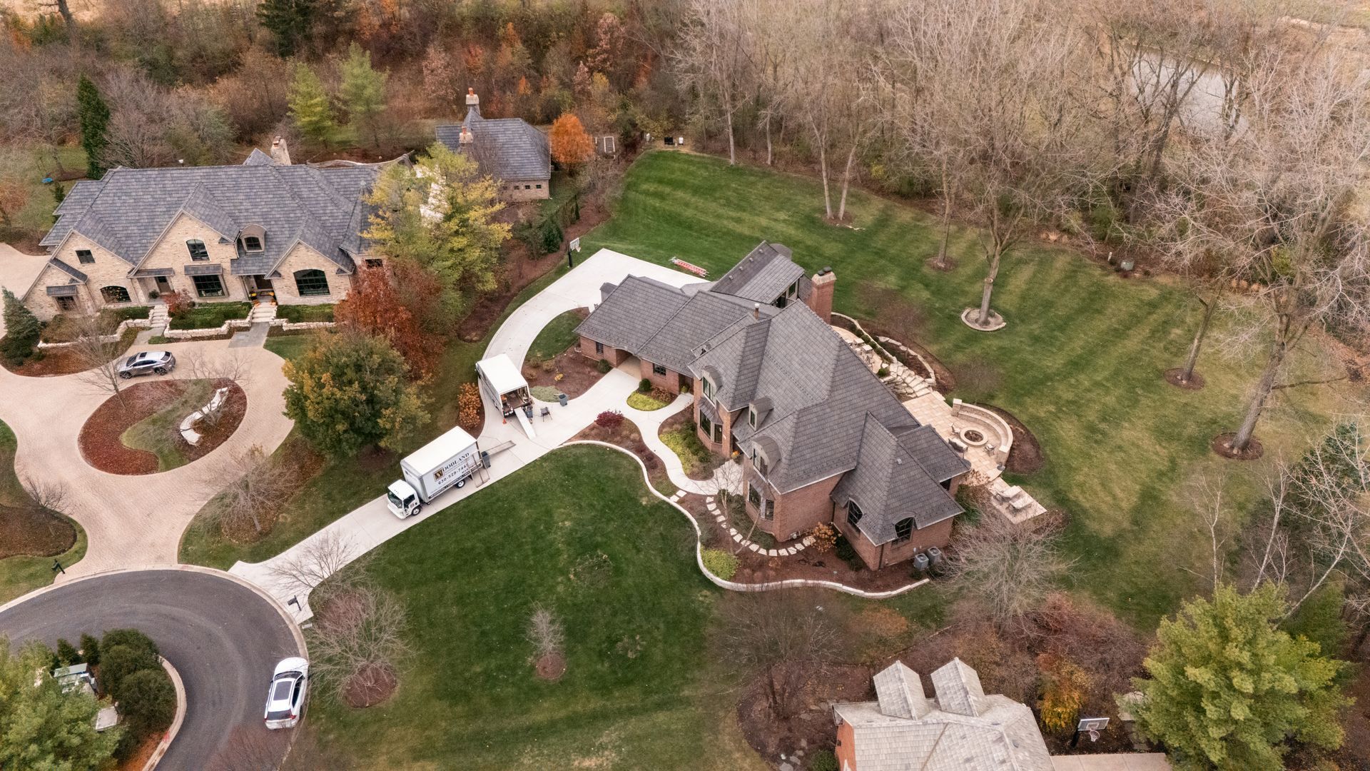 Aerial view of two large houses with long driveways, surrounded by trees and lawns.