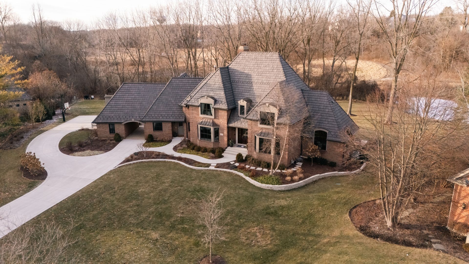 A large, brick house with a winding driveway and manicured lawn. Trees surround the property.