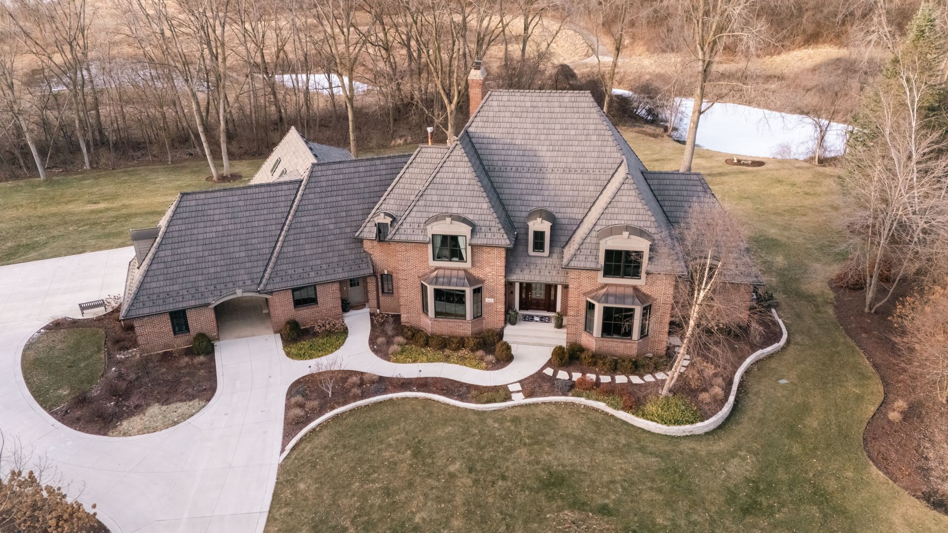 Drone view of a brick house with a curved driveway and landscaping.