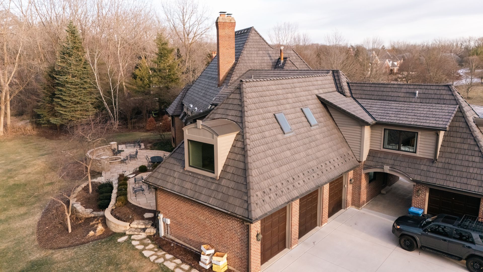 Aerial view of a brick house with a dark roof and a car parked in the driveway.