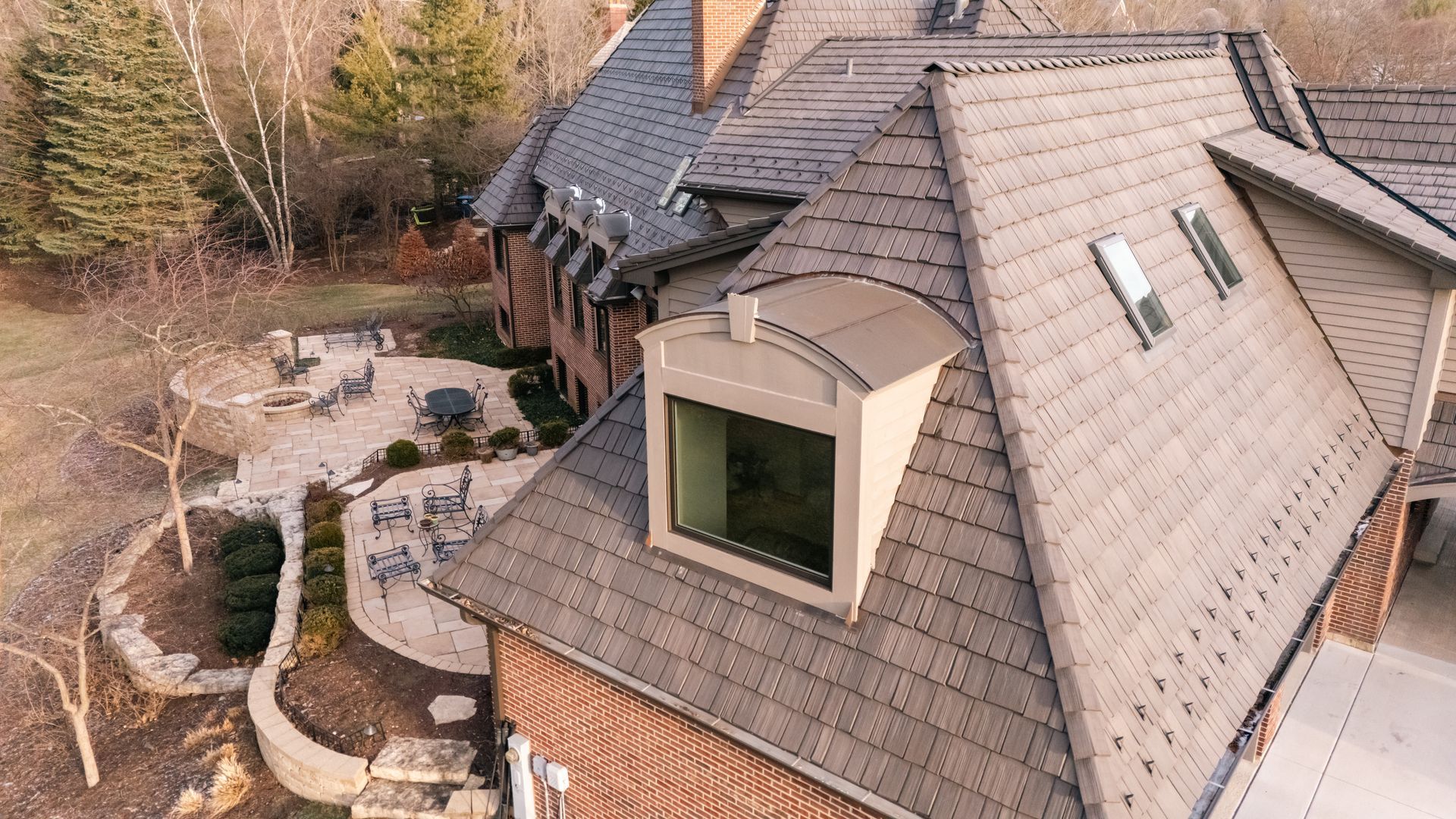 Brown roof of a large brick house with a windowed dormer. Outdoor patio visible below.