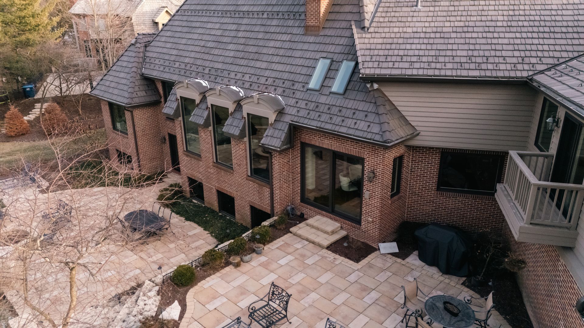 Brick home with stone patio, windows, and a gray roof.