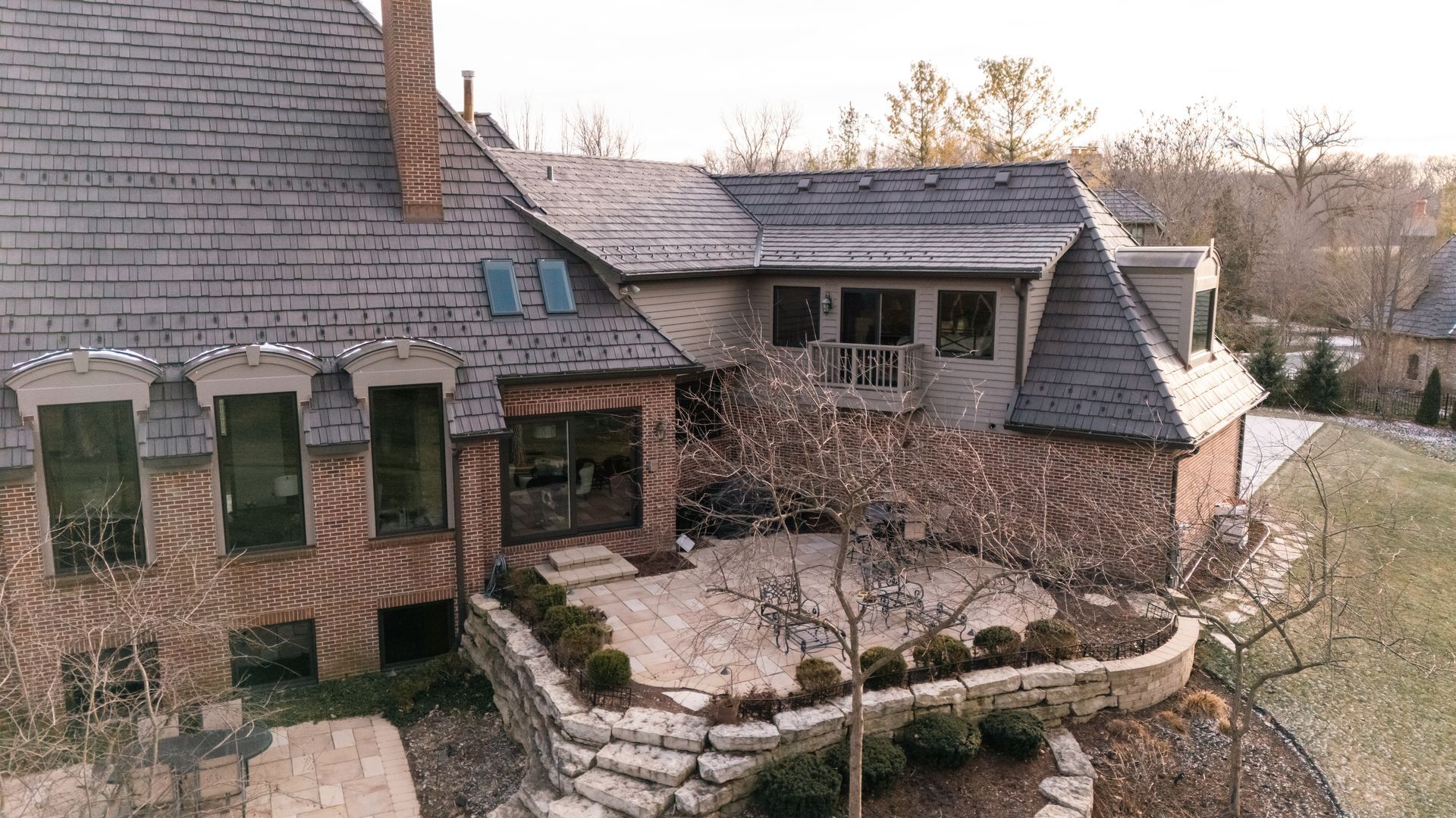 Brick and stone home with slate roof, patio, and landscaping.