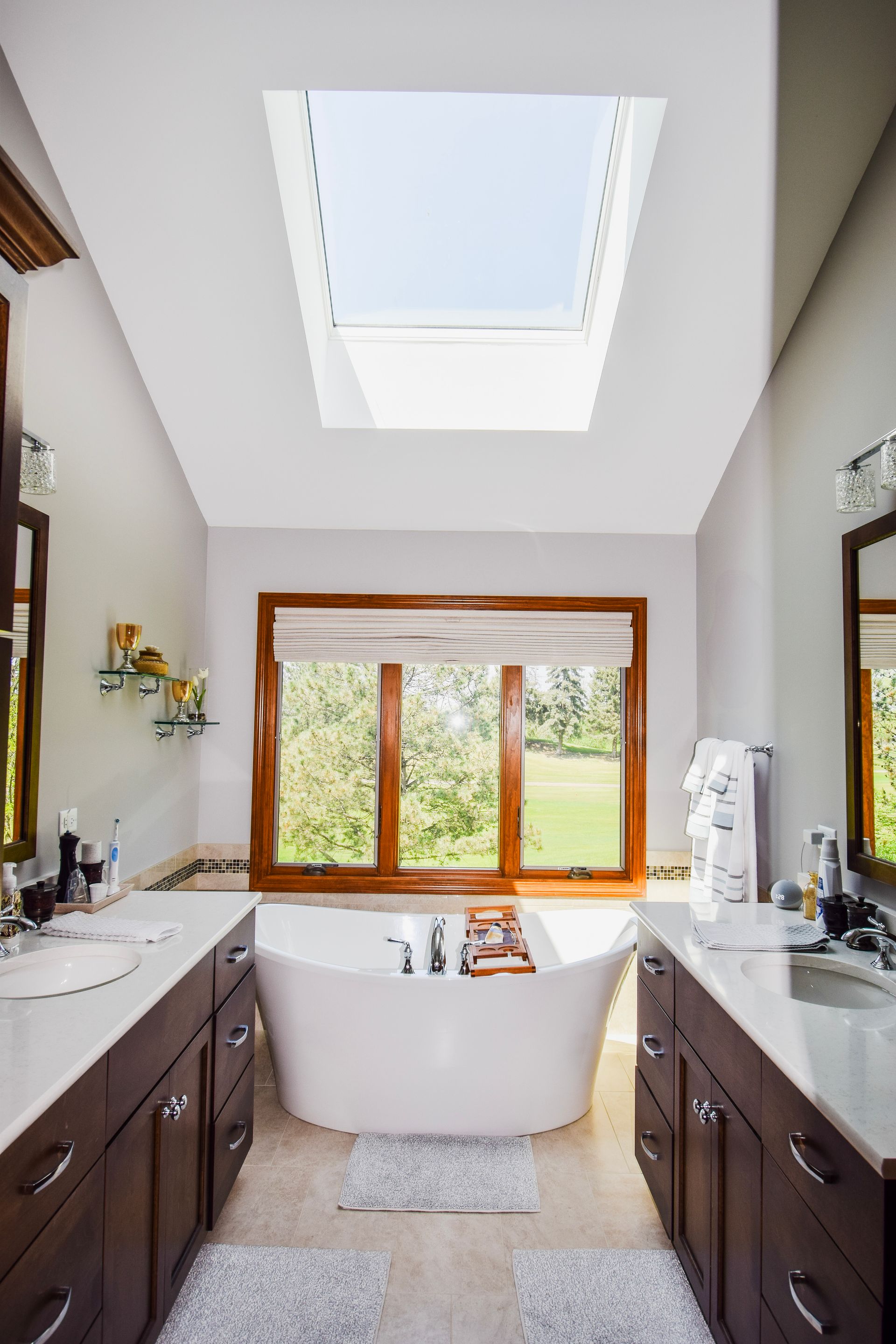 A bathroom with two sinks , a tub and a skylight.
