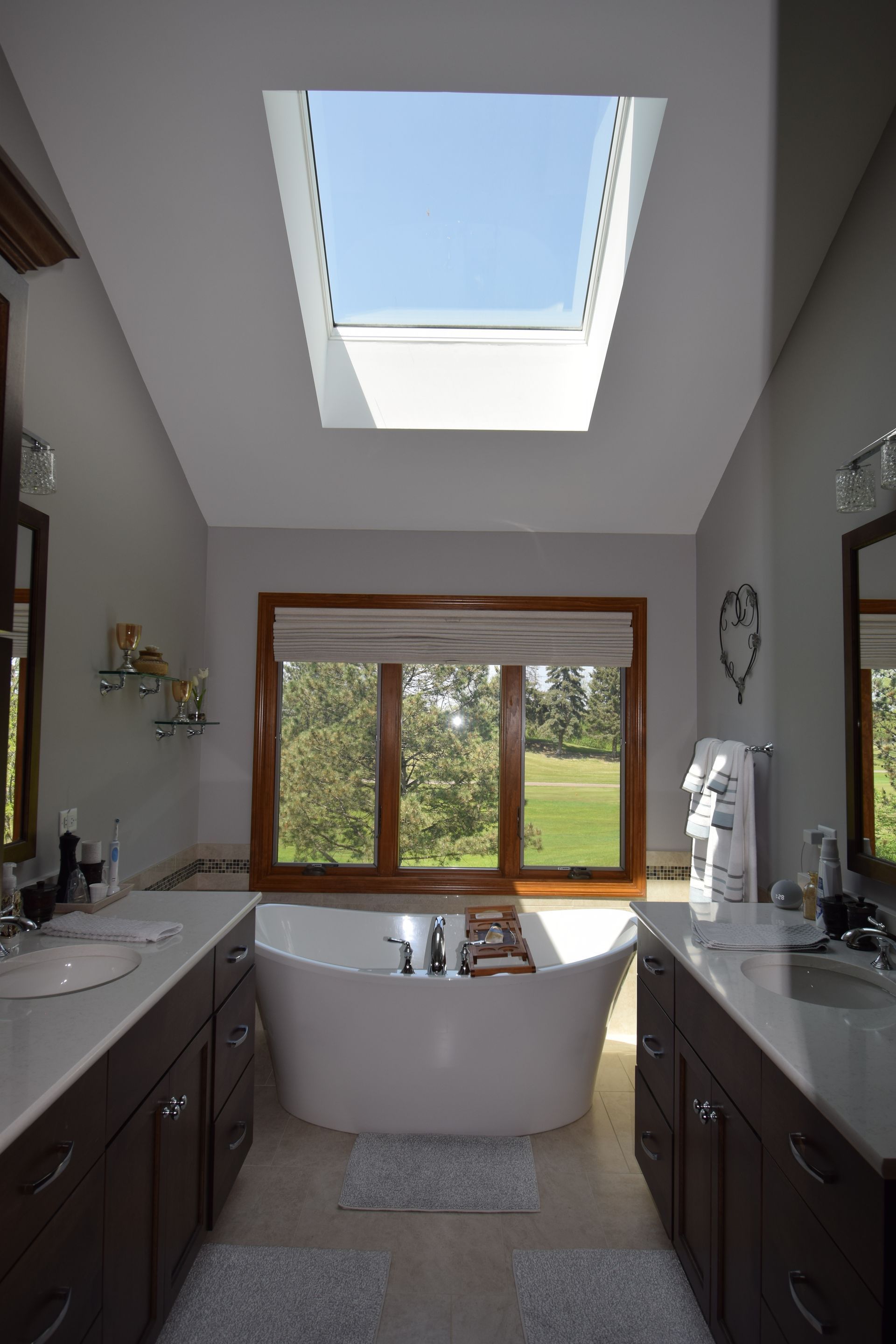 A bathroom with a skylight above the tub and two sinks.
