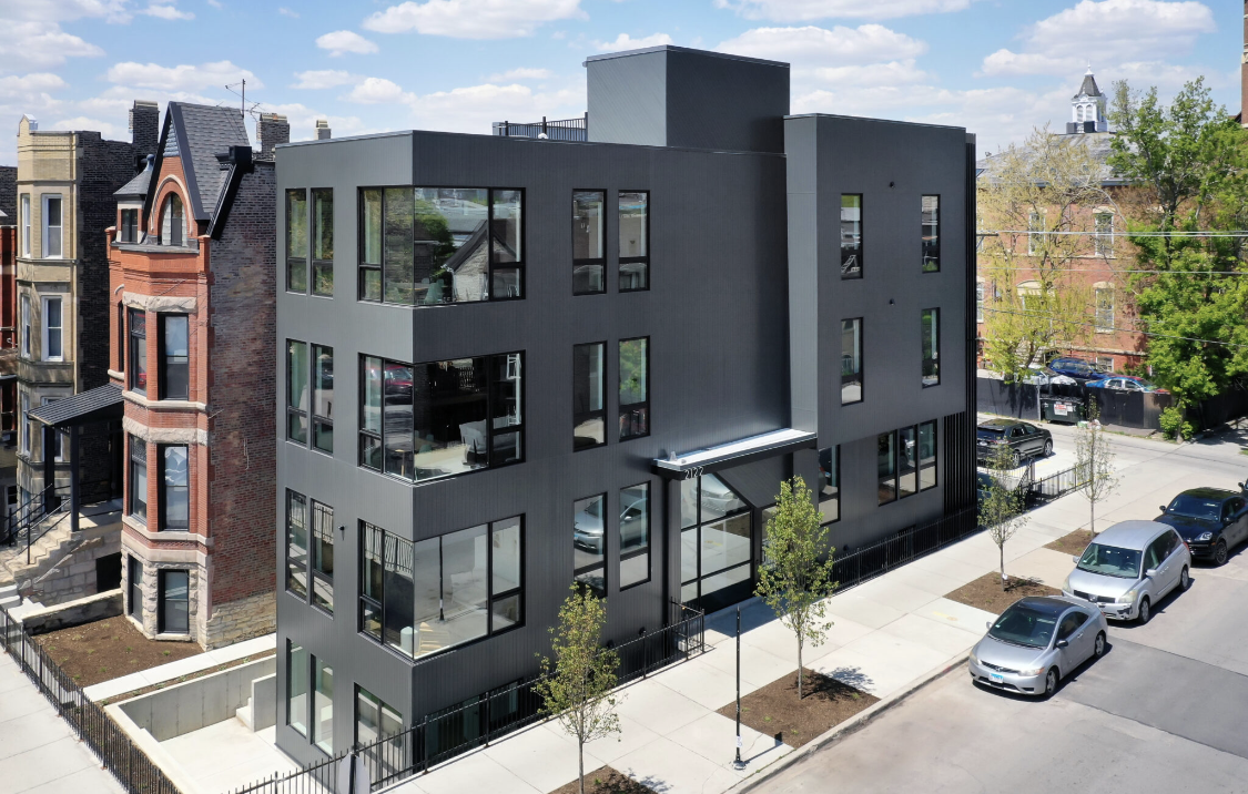 Modern black building with large windows next to a brick building on a city street.