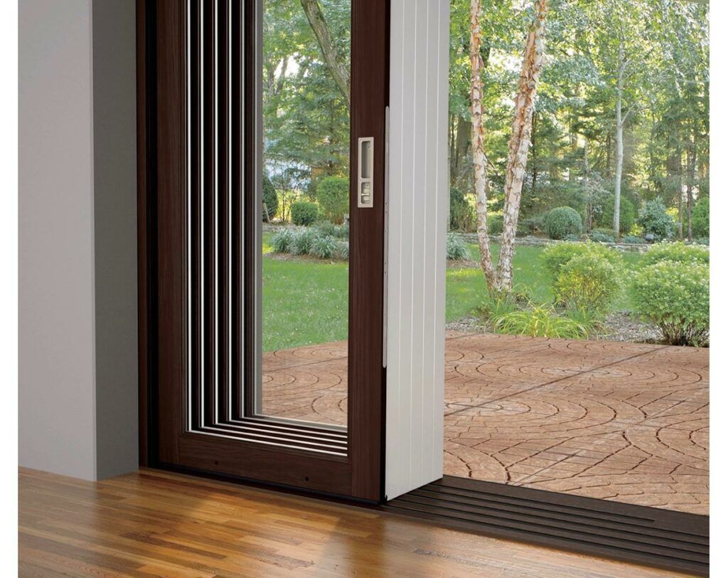 A sliding glass door is open to a patio with trees in the background.