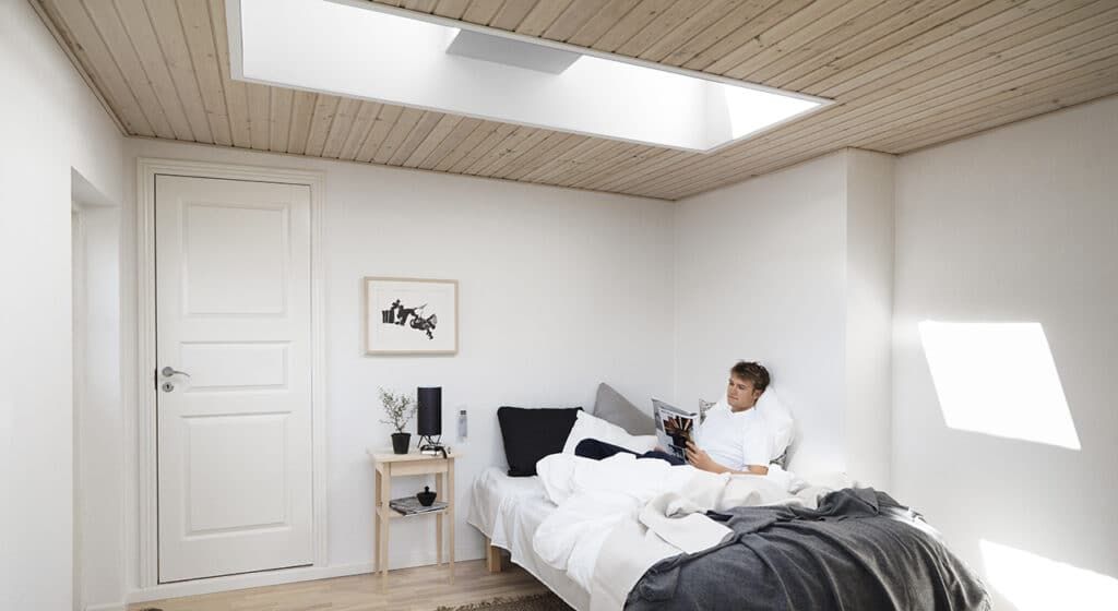 A man is sitting on a bed in a bedroom with a skylight.