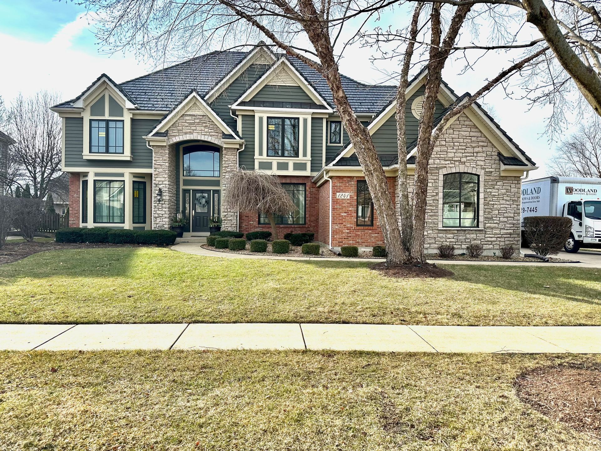 Two-story house with green siding, stone accents, and a moving truck parked nearby.