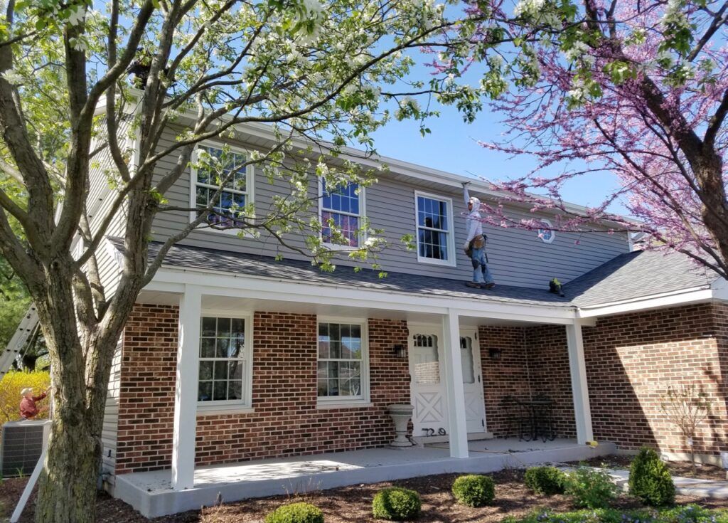 A brick house with a porch and a tree in front of it.