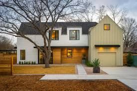 A white and yellow house with a garage and a tree in front of it.